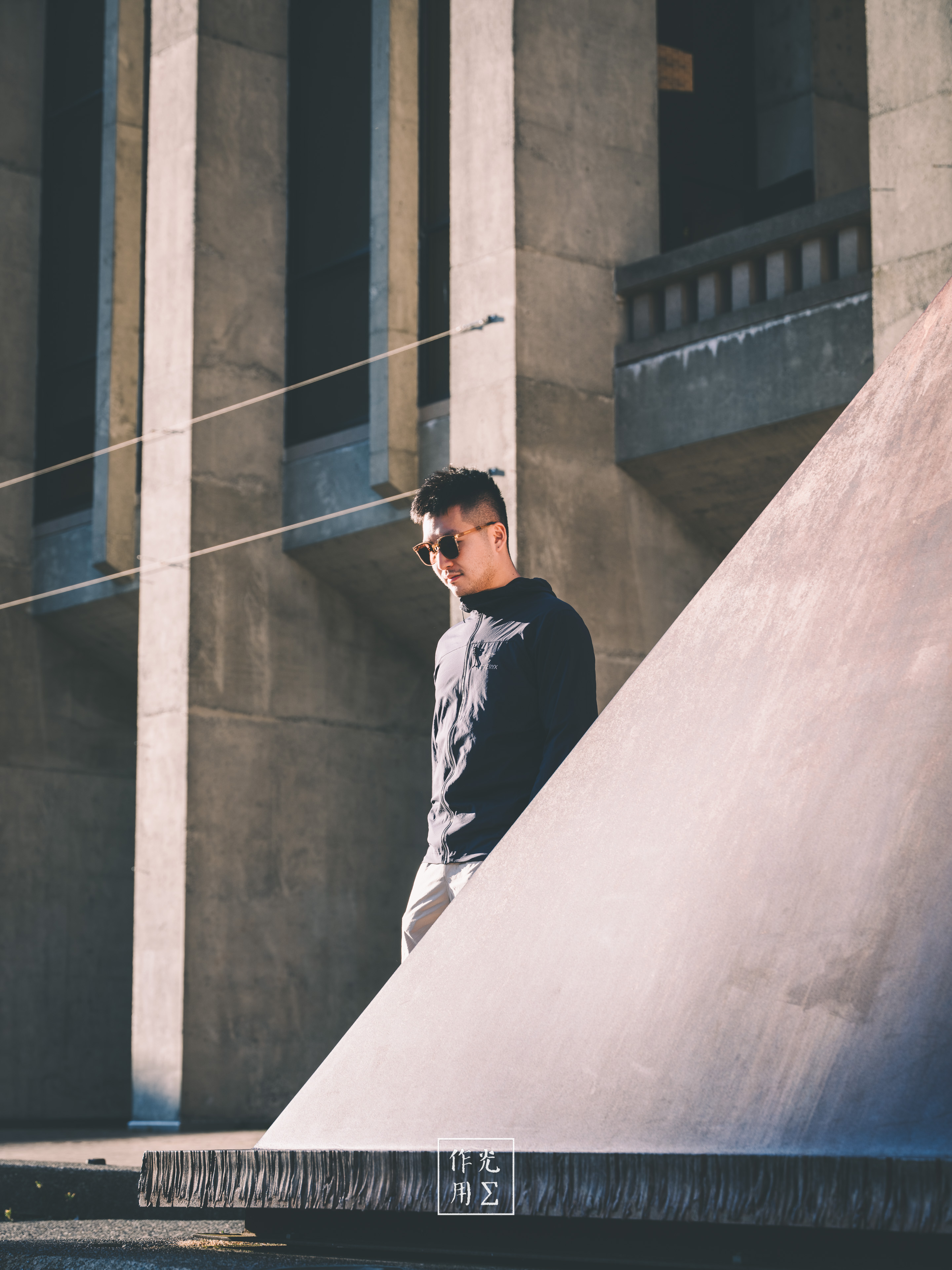 A young man stands amid monumental concrete columns and angular walls